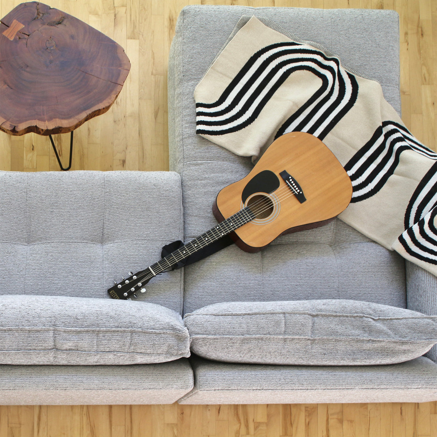 Overhead view of a grey sofa with a cotton throw and guitar