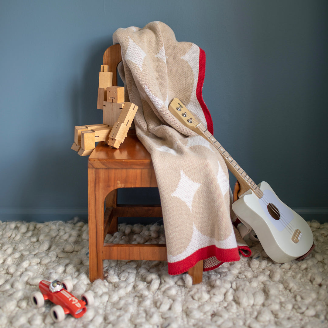 Beige and Red Cotton Baby Blanket on Chair with a Toy Guitar