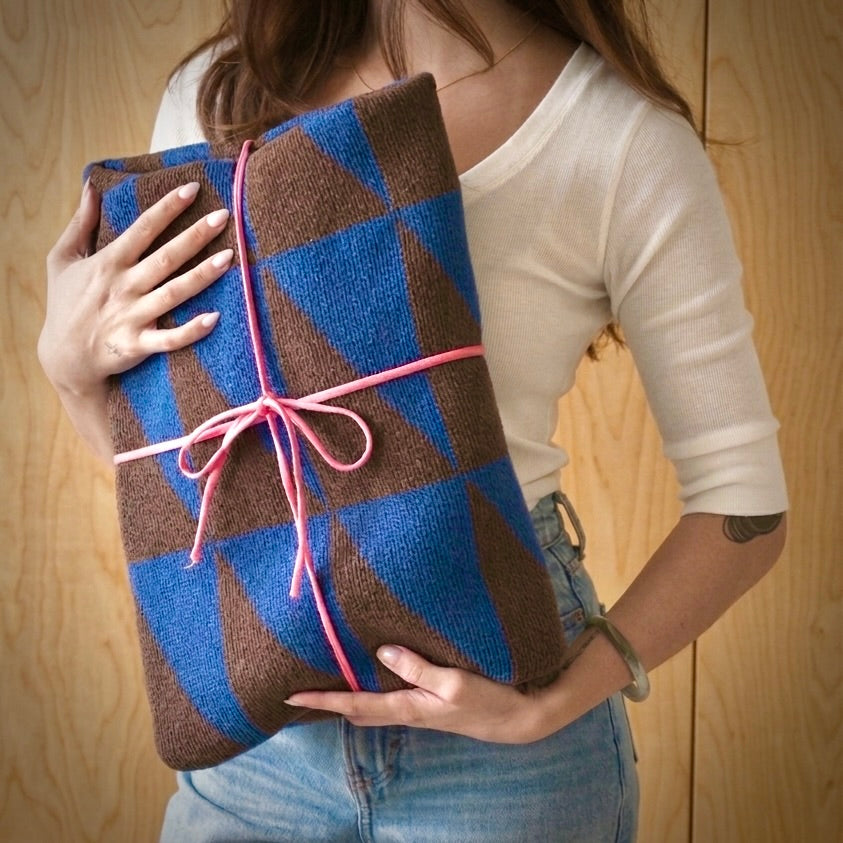 Woman holding a gift-wrapped modern patterned throw blanket with a bow, a thoughtful gift idea for someone whose love language is gifts.