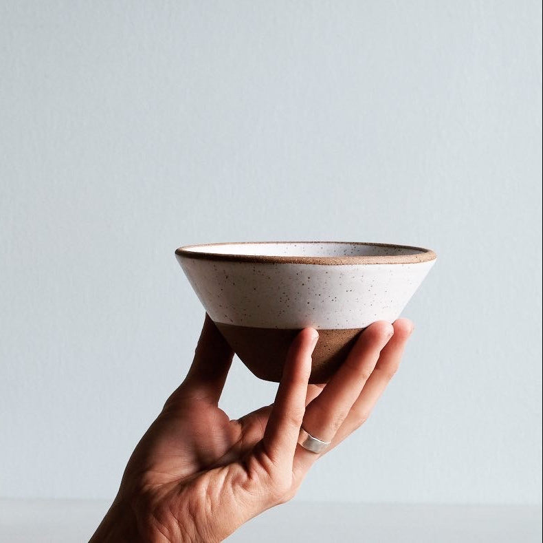 Hand holding a white and natural ceramic bowl on a light gray surface.