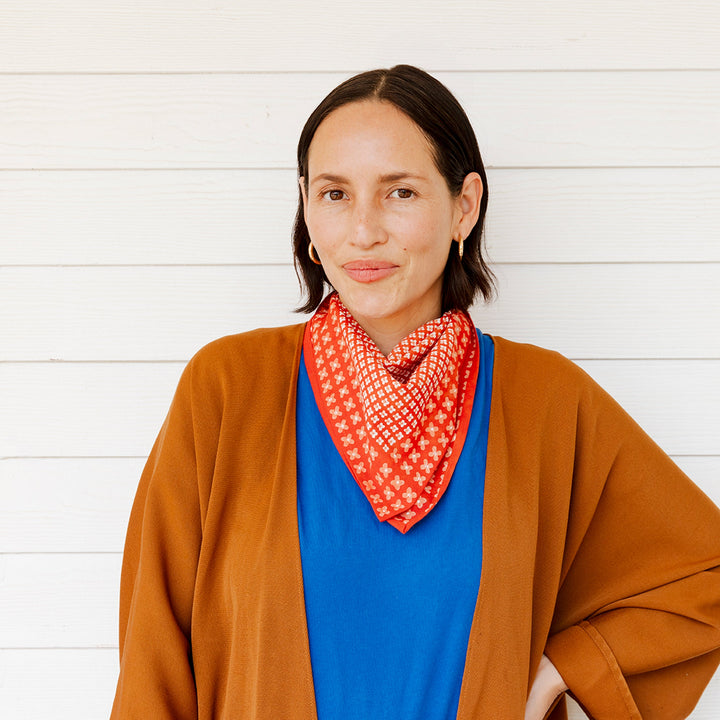 Woman wearing a brown cardigan, blue shirt, and red patterned scarf against a white background
