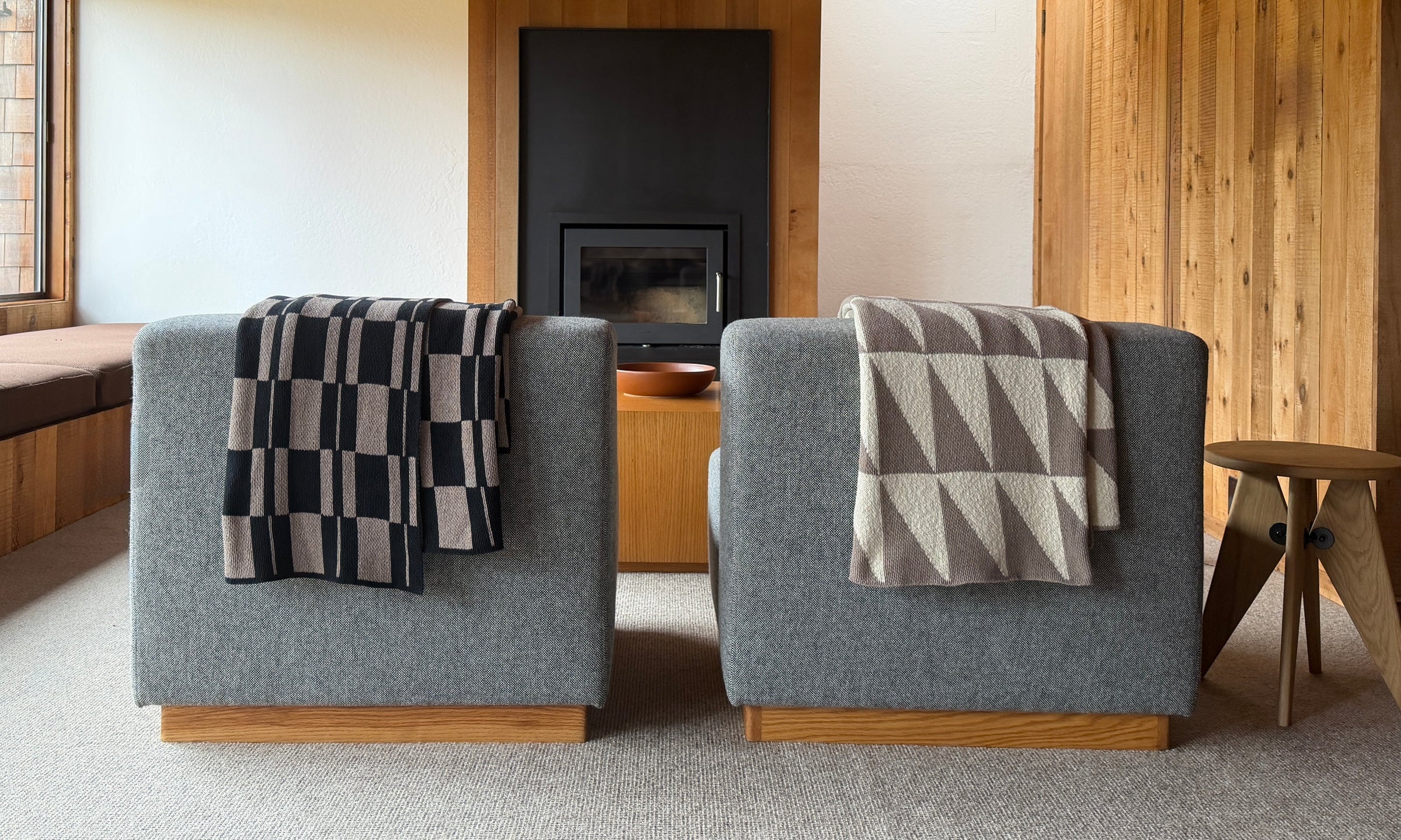Two gray chairs with patterned throws in a room with a fireplace and wooden walls.