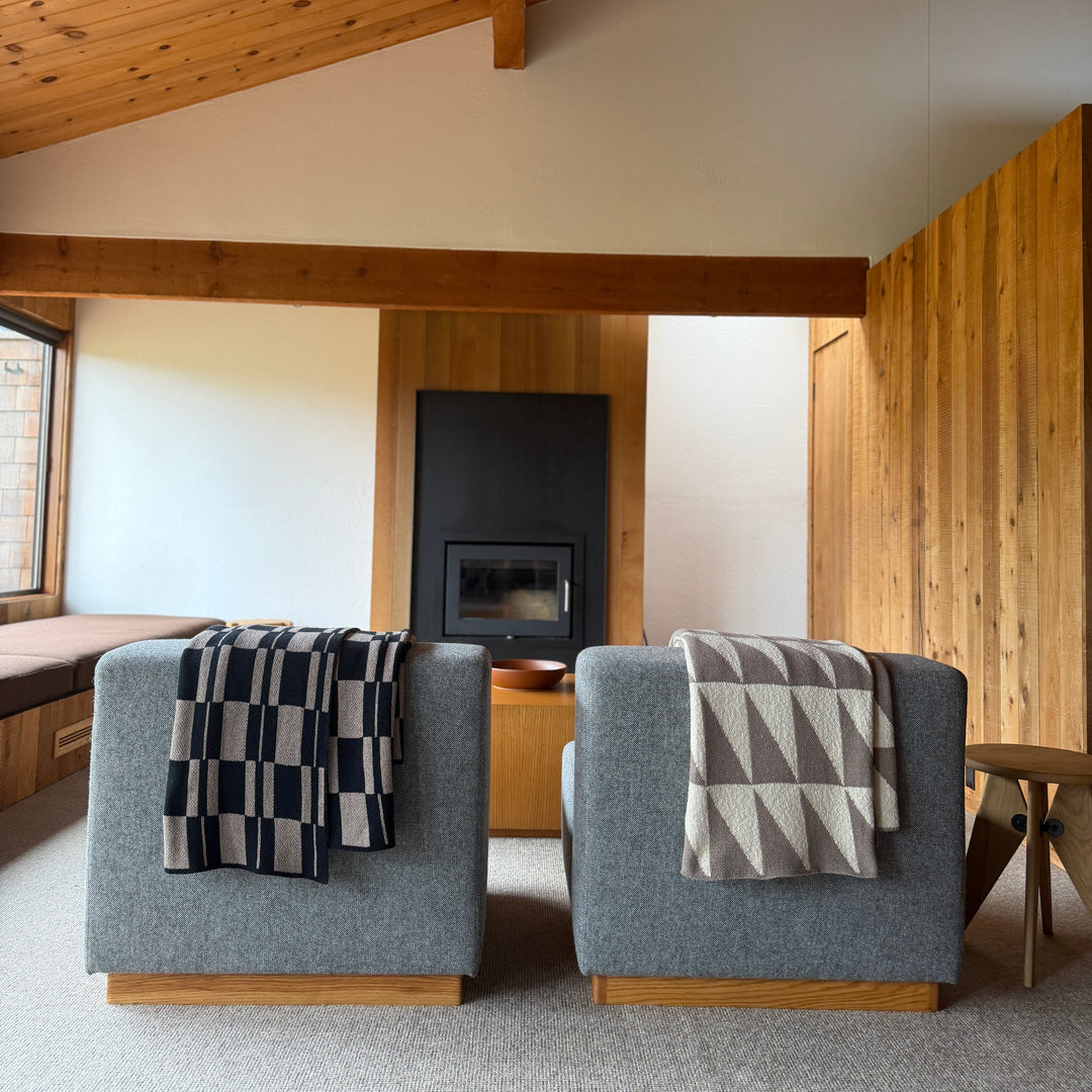 Two gray armchairs with patterned throw blankets in a modern room with wooden beams and a fireplace.