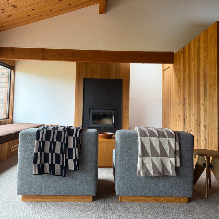Two gray armchairs with patterned throw blankets in a modern room with wooden beams and a fireplace.