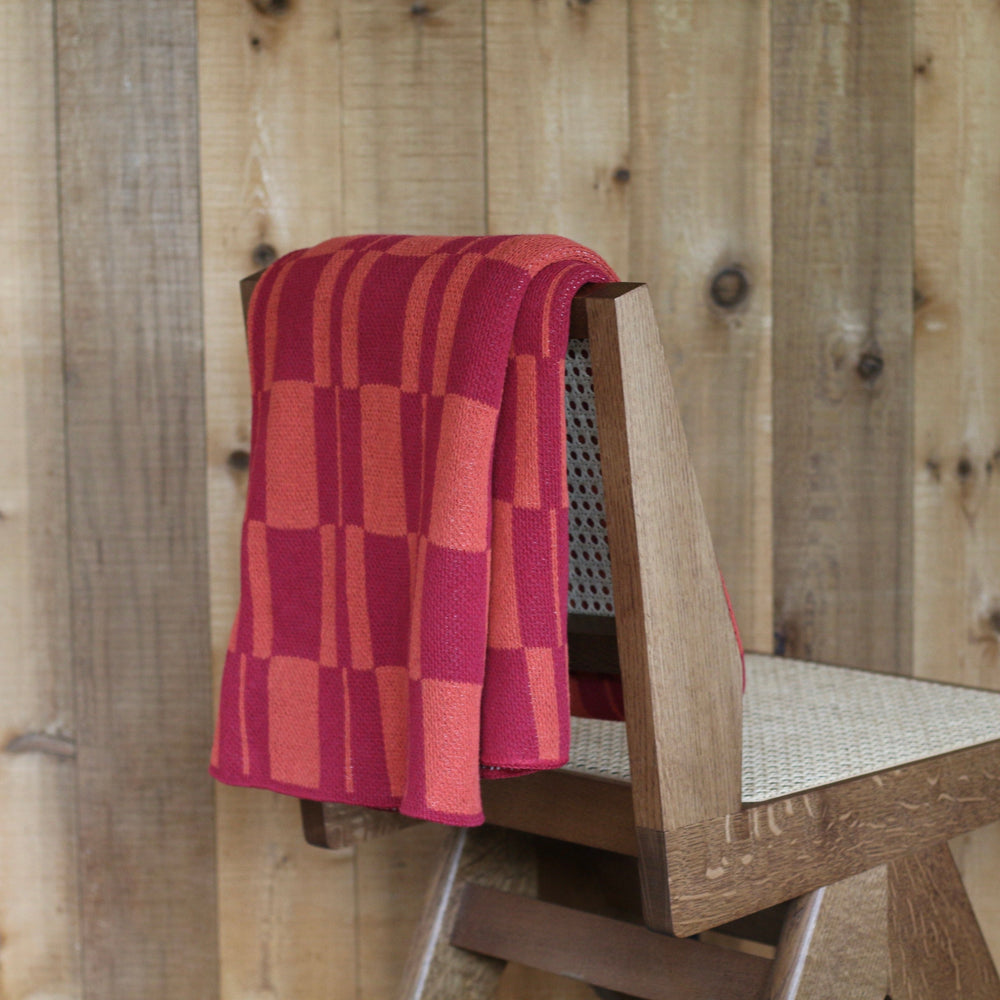 Wooden chair with a red checkered blanket against a wooden wall.
