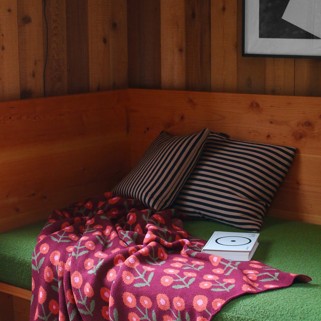 Nook with green cushion, striped pillows, and a floral blanket against wooden walls.