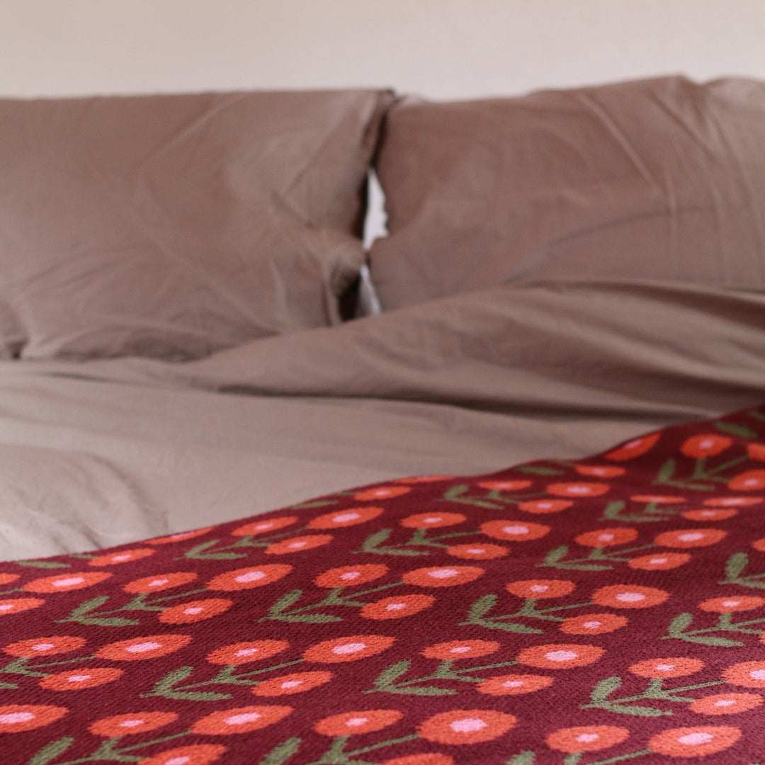 Close-up of a patterned throw with red flowers on a maroon background on a bed