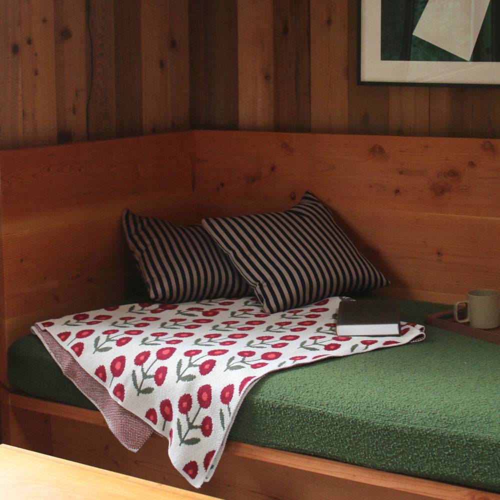 Wooden nook with a cushioned bench, striped pillows, and a floral blanket.