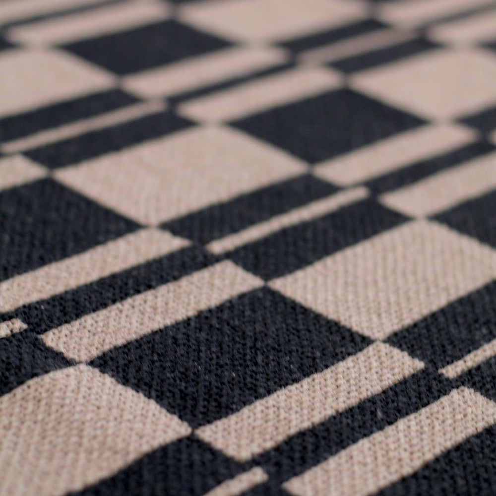 Close-up of a  pattern recycled cotton throw blanket with black and beige squares.