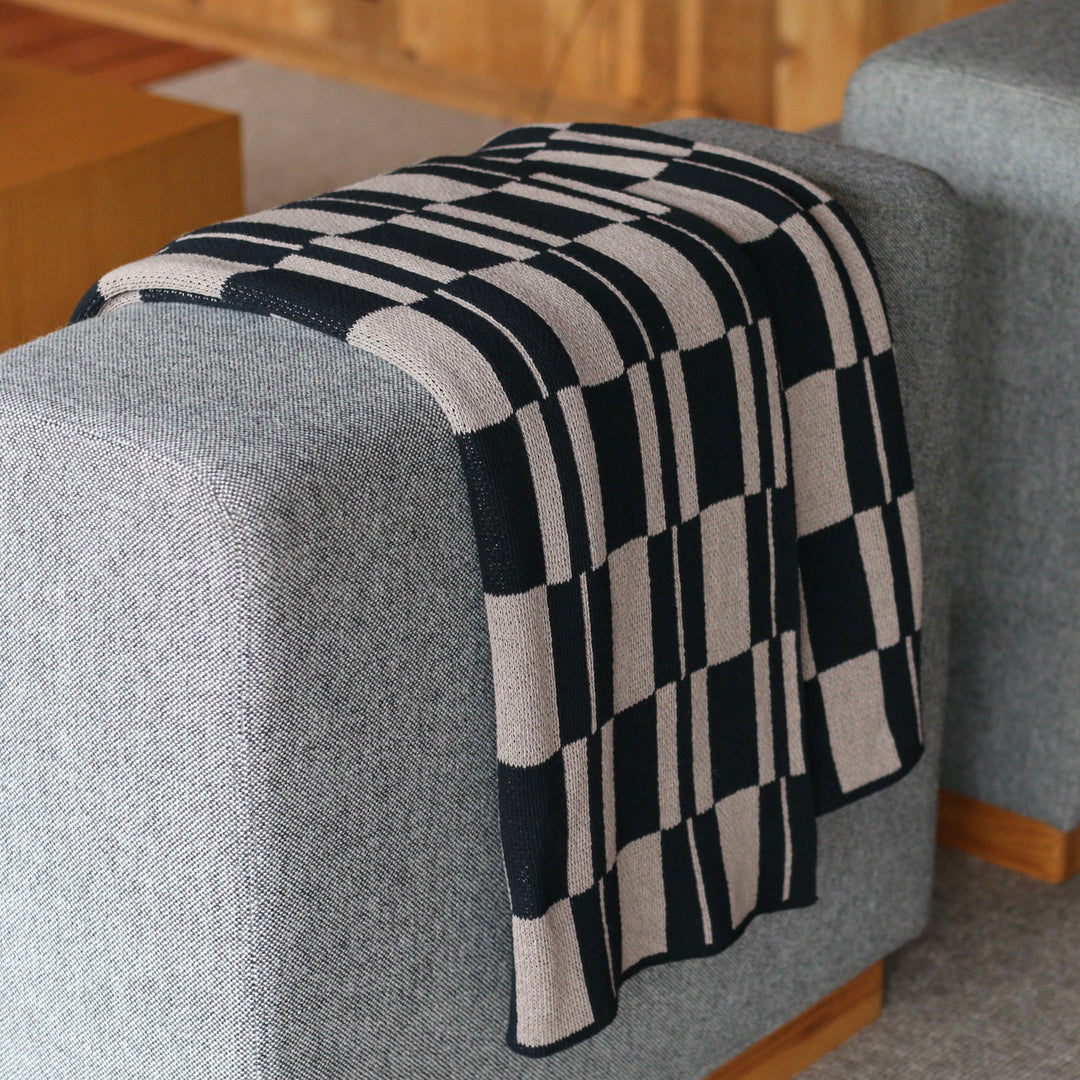 Checkered blanket draped over a gray armchair in a room with wooden furniture.