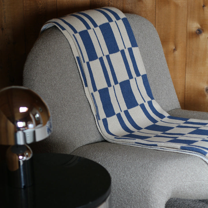 Cream chair with a blue and white patterned throw blanket draped over it, against a wooden wall.