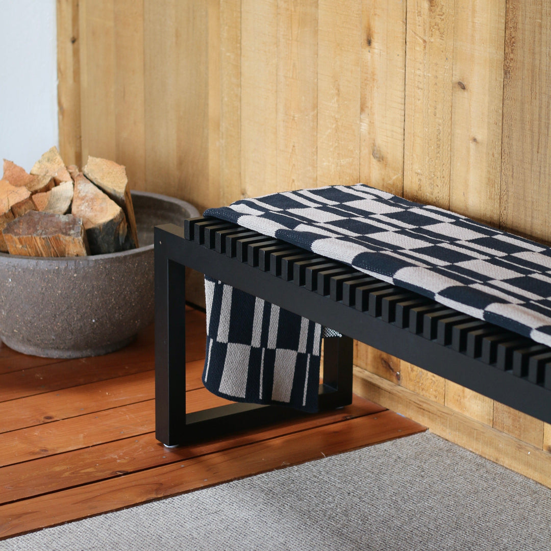 Black bench with a patterned cushion against a wooden wall.