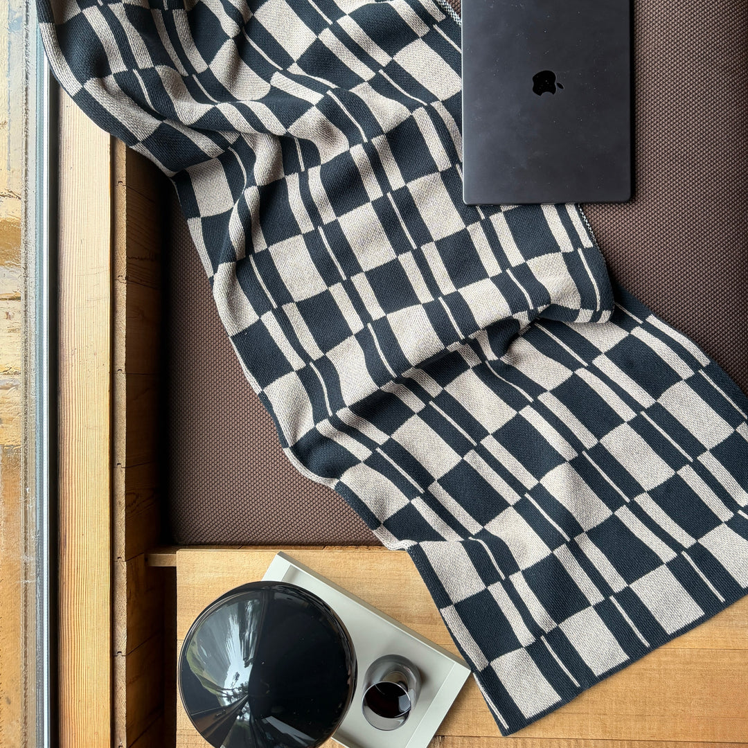 Black and Taupe checkered throw draped over a surface with a black electronic device on top.