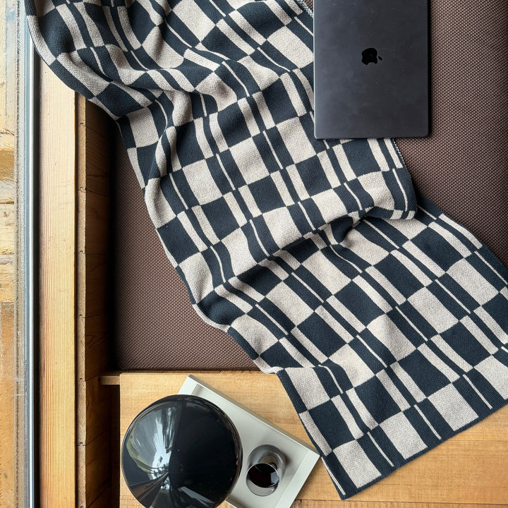 Black and Taupe checkered throw draped over a surface with a black electronic device on top.
