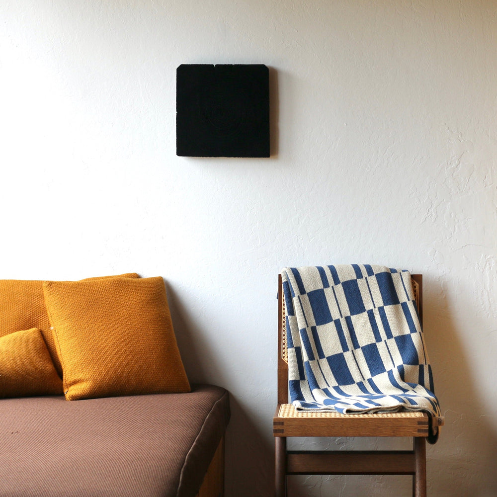 Sofa with yellow cushions and a chair with a blue and white patterned blanket against a white wall.
