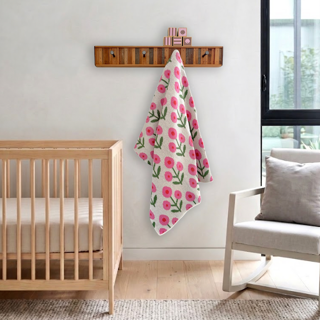 White baby blanket with pink flowers hanging on a hook rack in a simple modern baby nursery with a light wood crib and simple rocking chair