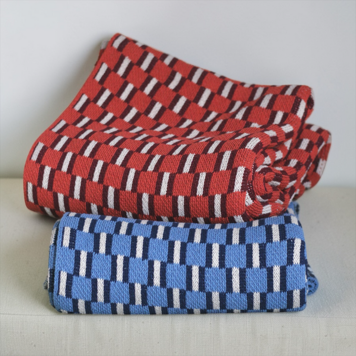 Two folded throws, one red and white checkered, the other blue and white checked, on a light surface.