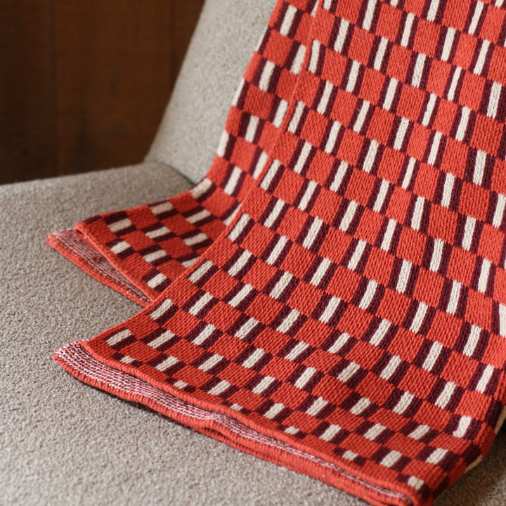 Folded orange and burgundy and white patterned throw blanket on a cream surface