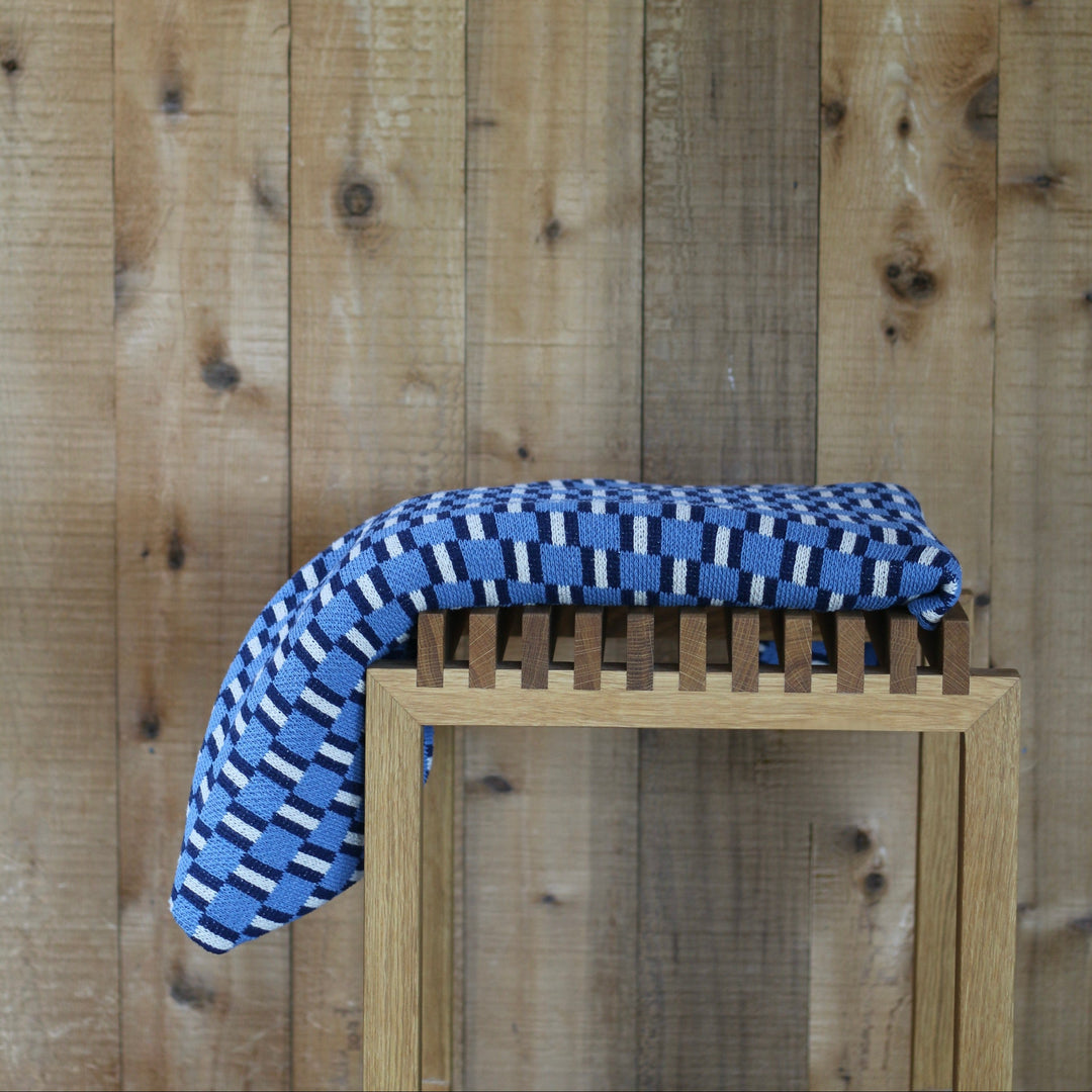 Blue and white patterned blanket draped over a wooden stool against a wooden wall.