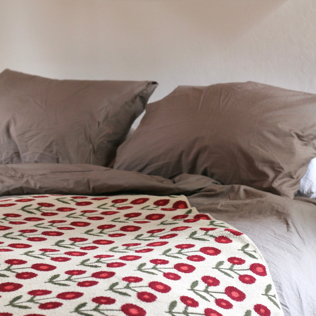 Bed with red and white floral blanket and gray pillows, framed artwork on wall.