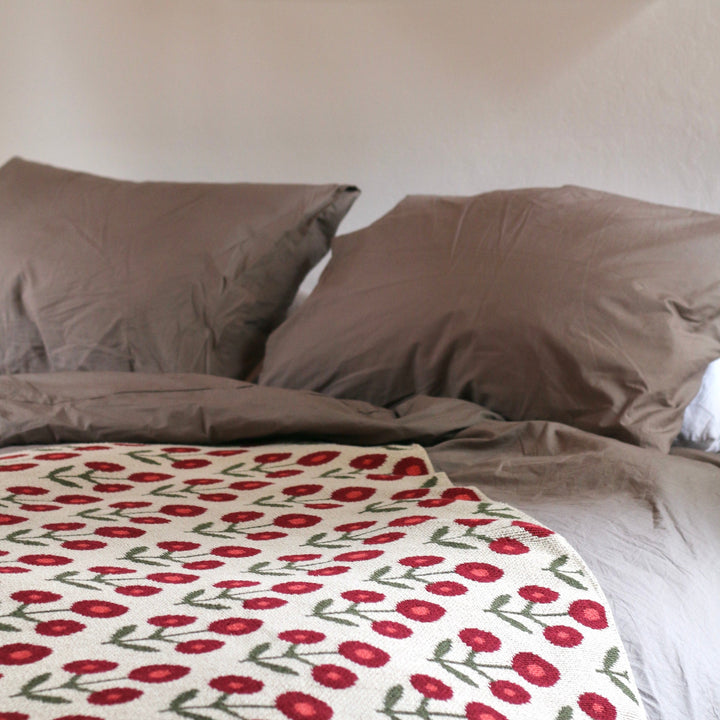 Bed with red and white floral blanket and gray pillows, framed artwork on wall.
