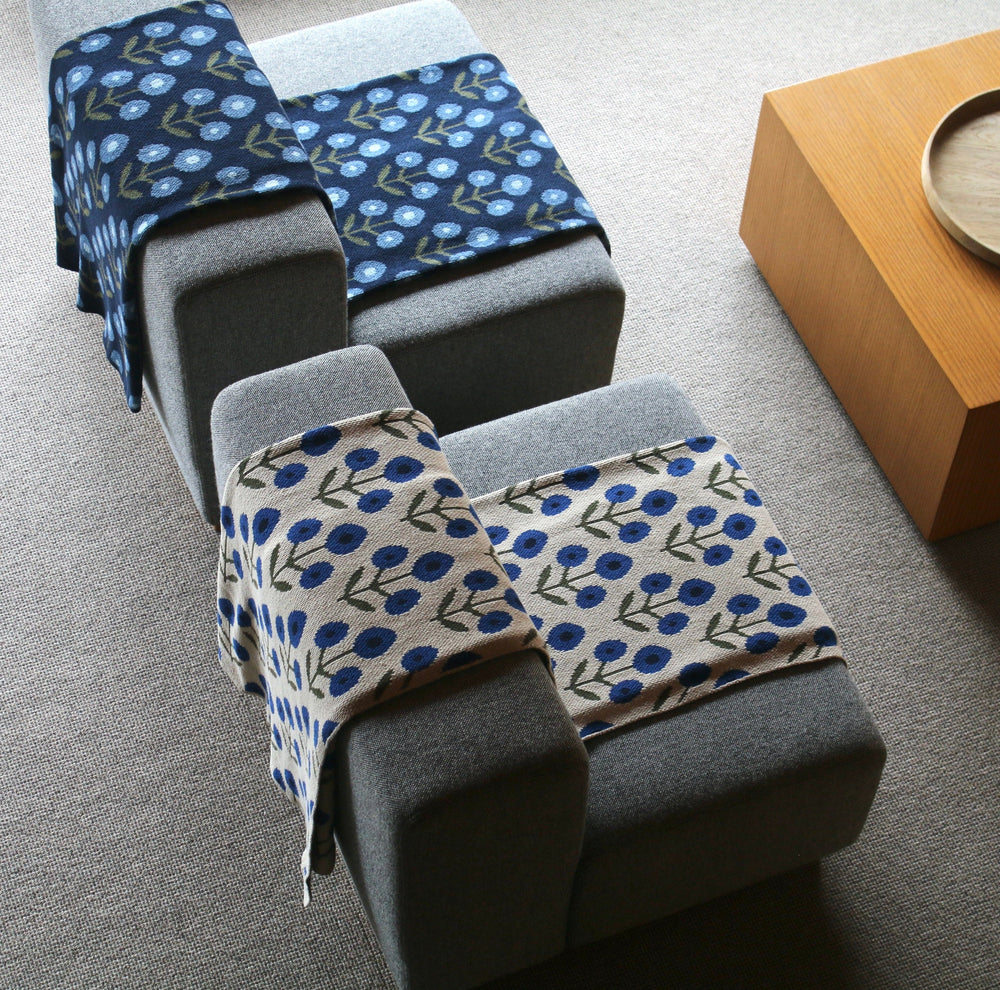 Gray armchair with blue patterned throw blankets and a wooden tray on a wood surface.