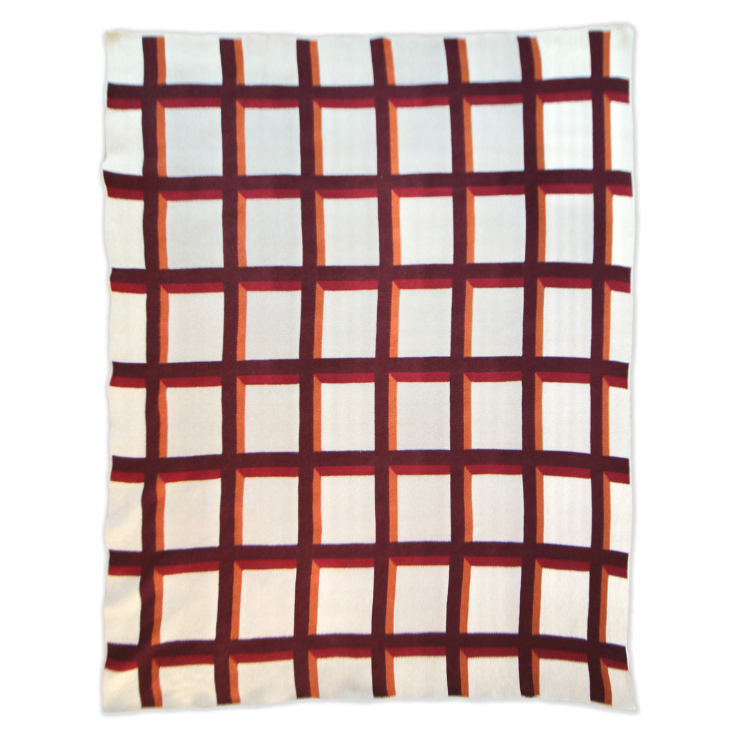 a throw blanket featuring a geometric grid pattern with alternating cream and white squares outlined by dark red and orange lines.