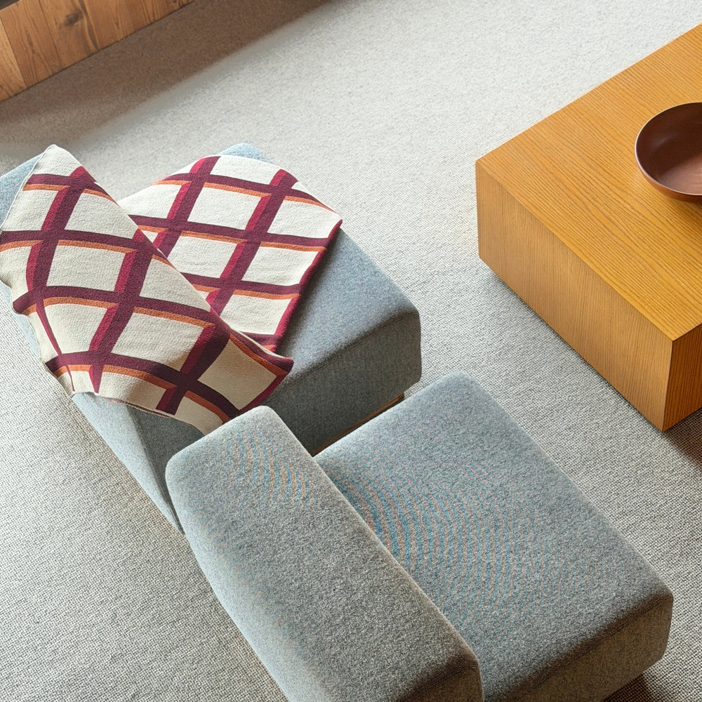 Gray upholstered bench with plaid cushion in a room with wooden coffee table and stool.