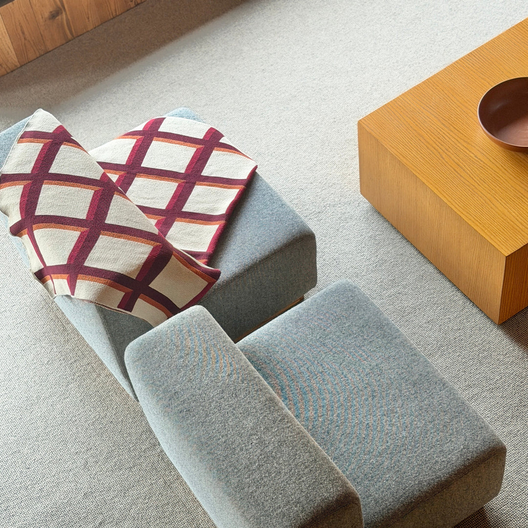 Gray upholstered bench with plaid cushion in a room with wooden coffee table and stool.