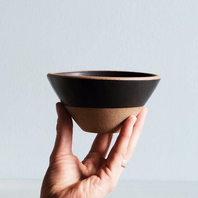 Hand holding a black ceramic bowl on a light gray background