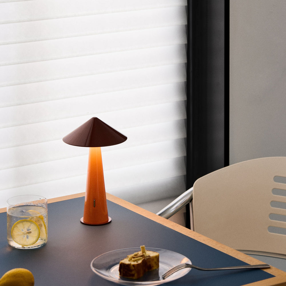 Table with a lamp, glass of water, lemon, and cake with a fork on a blue placemat.
