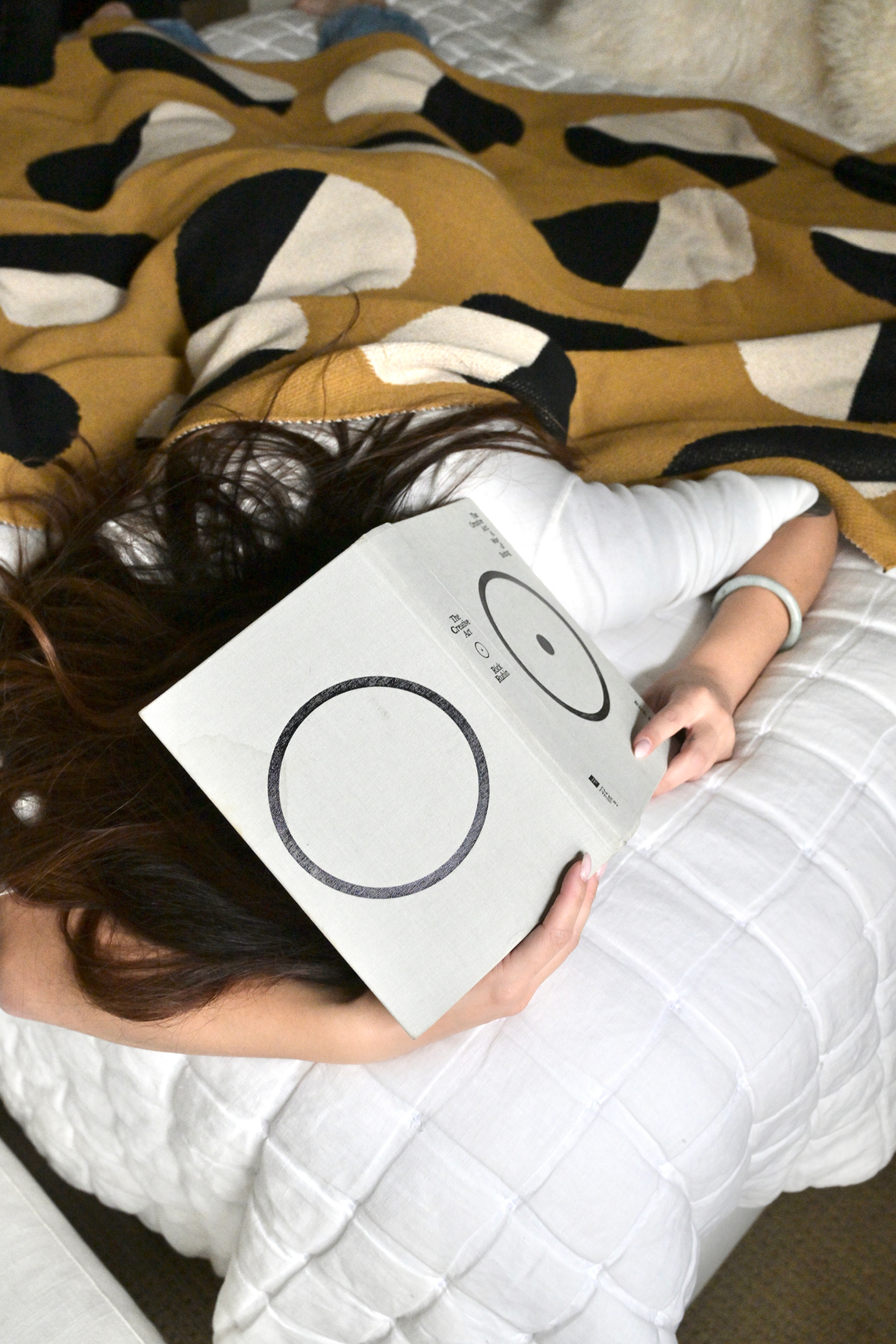 Person lying on a bed holding a book with a patterned blanket on them