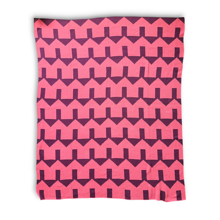 a throw blanket featuring a bold geometric house pattern of coral and dark red zig-zag stripes, shown flat against a white background.
