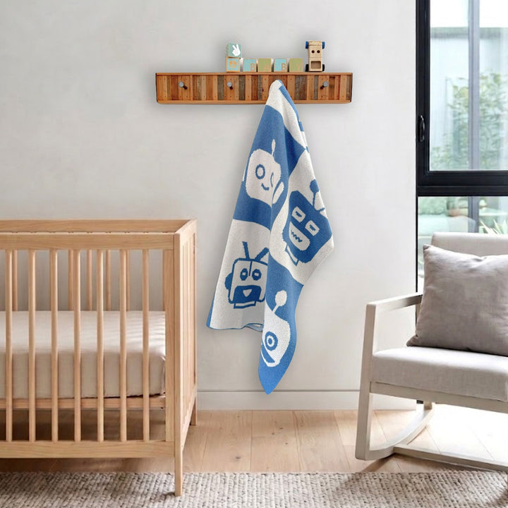 Blue and White Robot Faces Baby Blanket Hanging from a Wooden Hook Rack in a baby nursery with a light wood crib and rocking chair