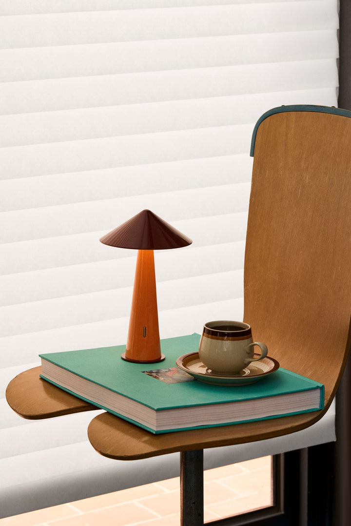Small wooden table with a lamp, book, and cup on a chair against a white wall.