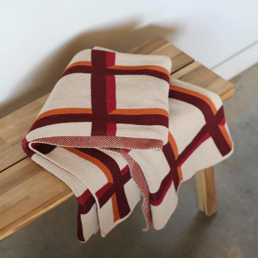 Plaid blanket draped over a wooden stool with a neutral background