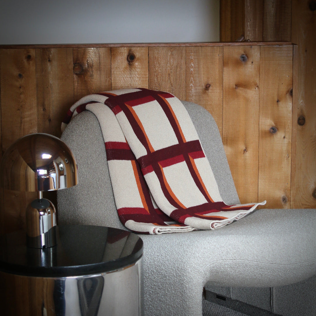 Gray chair with a grid pattern blanket against a wooden wall