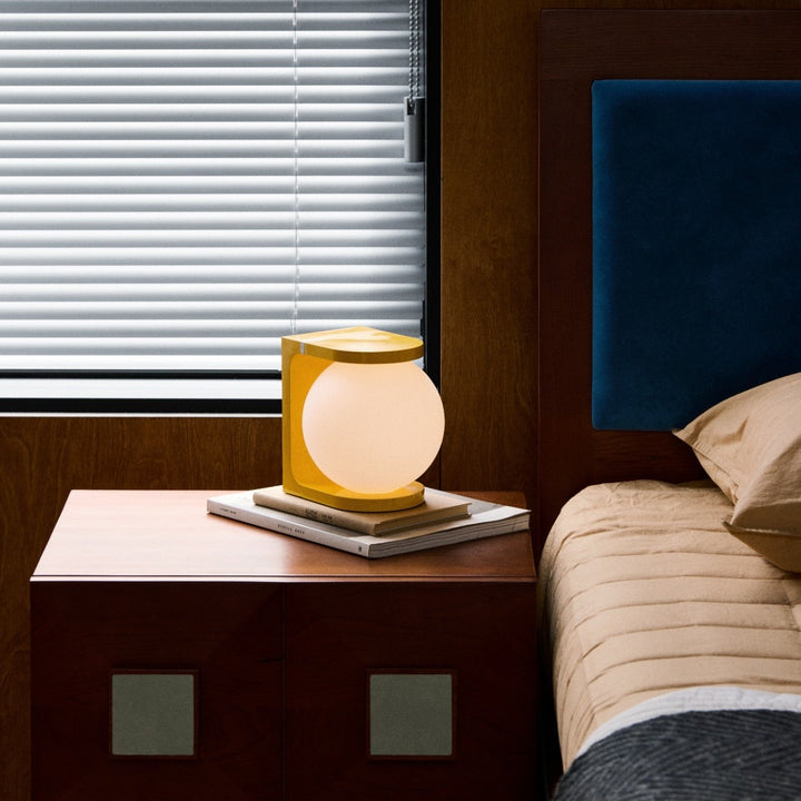 Lamp on a nightstand next to a bed with a window in the background